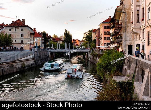 The promenade on the Ljubljanica river in the slovenian capital city Ljubljana with the Cobblers bridge and tourist boats on sunny day in summer with clouds
