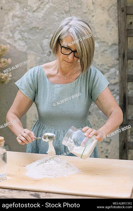 Mature woman with spoon preparing dough at back yard