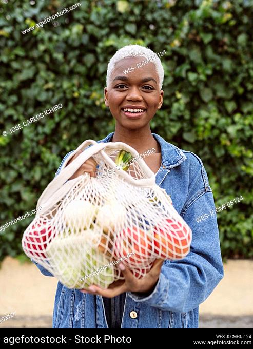 Smiling woman holding mesh bag with groceries