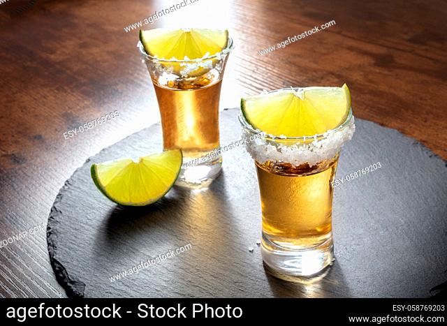 Tequila shots with salt rims and lime slices, served on a black slate tray