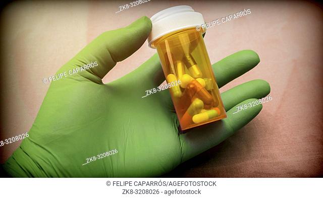 Nurse supports capsules bottle with left hand with glove of green latex in a hospital