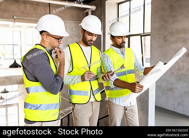 architects in helmets with blueprint at office