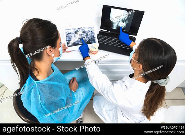 Young dentists discussing over x-ray image and using laptop at clinic