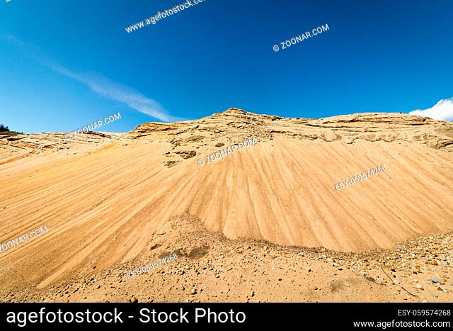 Hills in a sand pit, looks like a mountain. Blue sky and small white clouds in the background