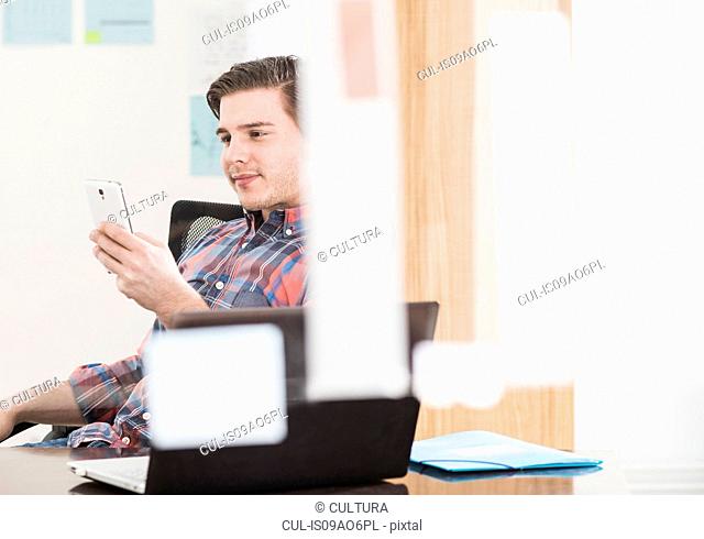 Young businessman looking at smartphone at office desk