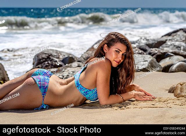A gorgeous brunette bikini model lounging on the shoreline at the beach on a sunny day
