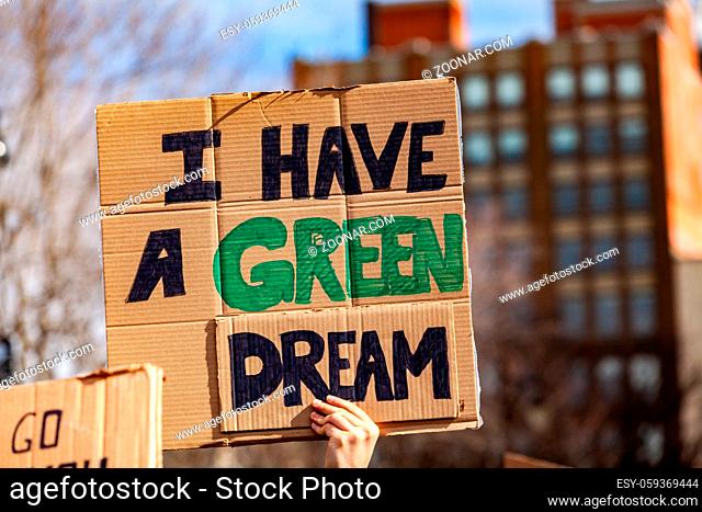 A protestor holds a cardboard sign, reading I have a green dream, viewed close-up as people unite against global warming in a city center