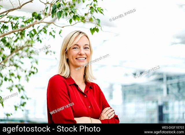Smiling businesswoman with arms crossed in front of plant