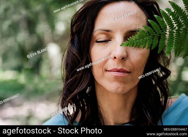 Woman with eyes closed holding fern leaf in forest