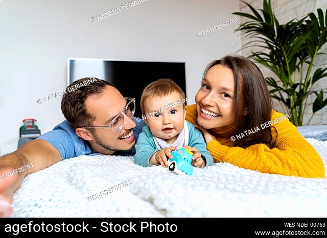 Cute baby boy with parents lying on couch at home