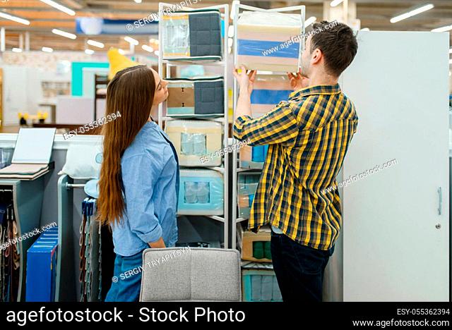 Young love couple choosing core of mattress in furniture store showroom. Man and woman looking samples for bedroom in shop