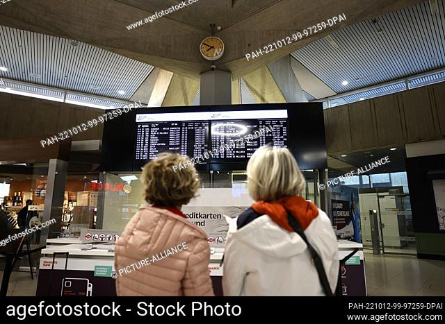 06 October 2022, North Rhine-Westphalia, Cologne: Two travelers stand in front of a display showing the cancelled flights