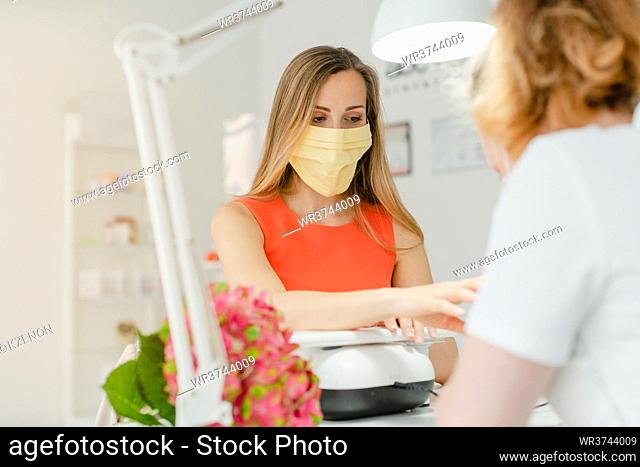 Woman in the nail salon receiving manicure wearing a face mask during coronavirus crisis