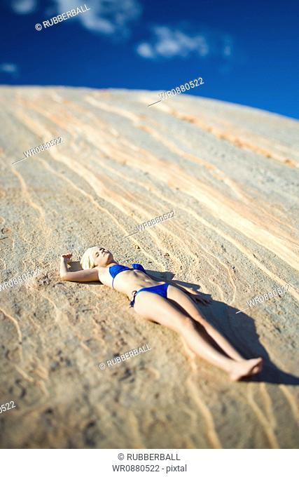 High angle view of a young woman sunbathing on a rock