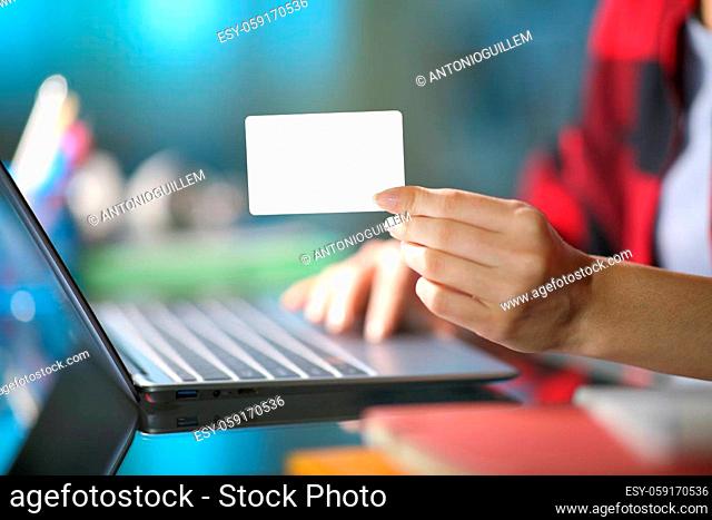 Close up of a student hand showing blank credit card using laptop at home in the night