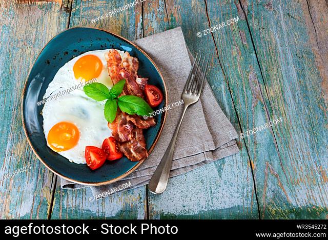 Breakfast consists of fried eggs, bacon and vegetables on the old wooden table, rustic style