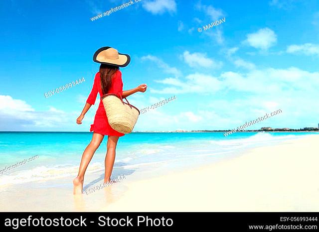Beachwear woman tourist with straw sun hat and beach bag walking on tropical summer vacation wearing sunhat and red tunic dress cover-up relaxing on travel...