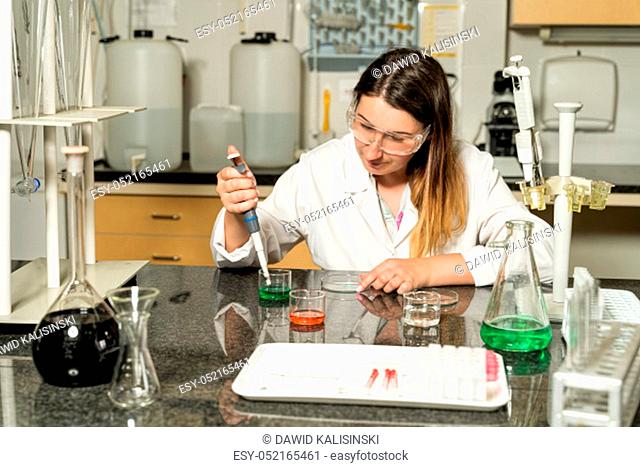 Middle age, Caucasian white, female laboratory technician in white robe sampling with pipette chemical liquid solution in laboratory