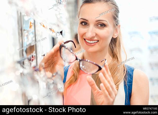 Beautiful woman in optician store chooses her glasses looking pleased