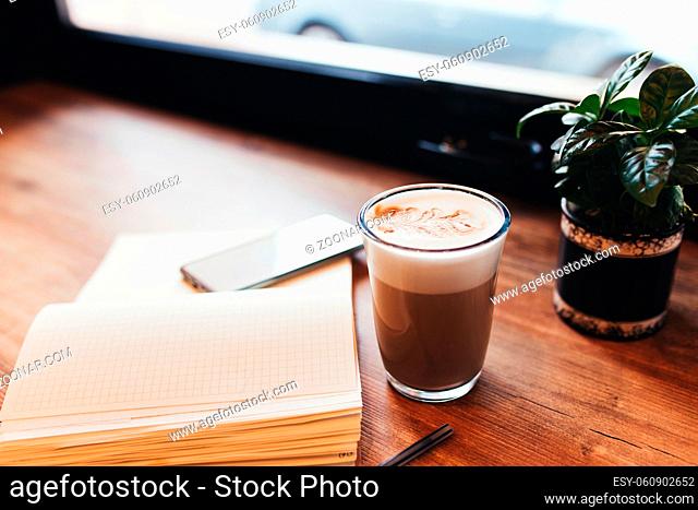 Cup of coffee, notebook, phone at table in cafe. Blurred background. High quality photo