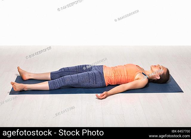 Beautiful sporty fit yogini woman relaxes in yoga asana Savasana, corpse pose in studio