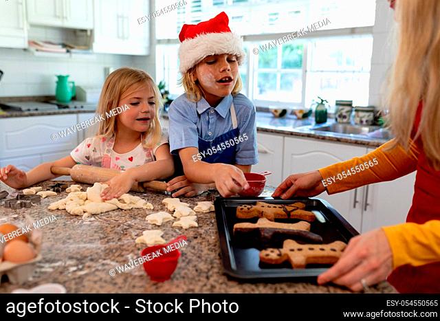 Front view of a young Caucasian mother with her young daughter and son in their kitchen at Christmas time making cookies together
