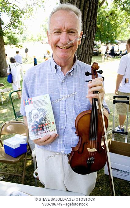 Author G  R  Revelle holds book My Enemy's Child and violin  Swedish Svenskarnas Dag Minnehaha Park Minneapolis Minnesota USA