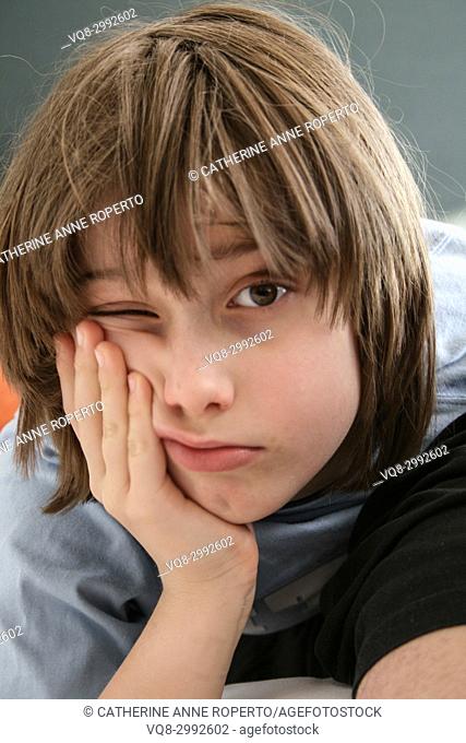 Young boy with messy brown hair leaning his cheek on his hand with one eye open in Brussels, Belgium