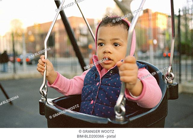 Mixed race girl swinging in playground