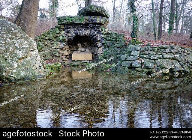 23 December 2022, Thuringia, Weimar: The sphinx resting on a stone cube and the surrounding stones are reflected in the park on the Ilm River by the water...