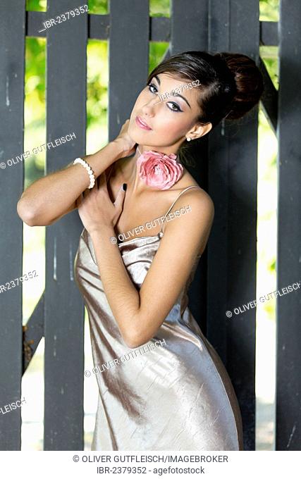 Young woman with an updo hairstyle and a silvery evening dress posing in front of a grey wooden gate