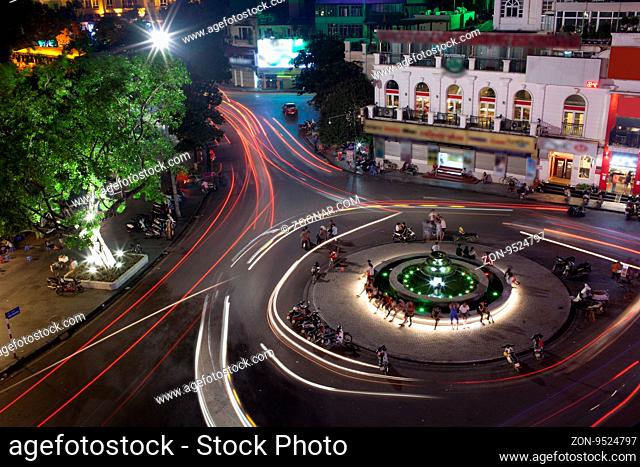Night view of illuminated fountain on the city square and transport moving around it. White and red traffic traces in motion