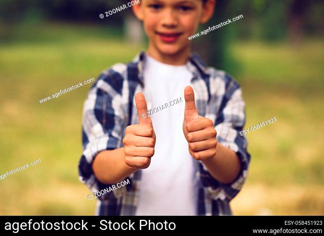 Adorable little boy showing thumbs up. Cute smiling boy wearing white and blue button up and white shirt underneath showing thumbs up with both of his hands