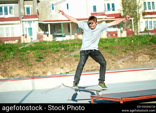 The young guy slides on a skateboard in a manual on a ramp on the background of houses
