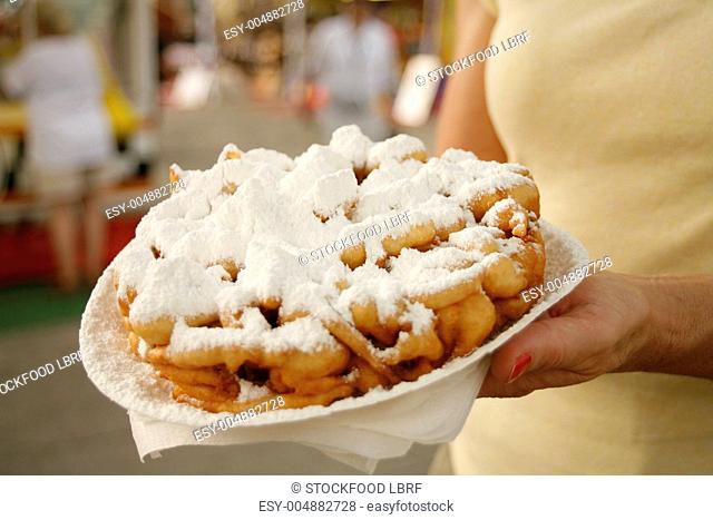 A woman holding a plate of funnel cakes covered in icing sugar at a market
