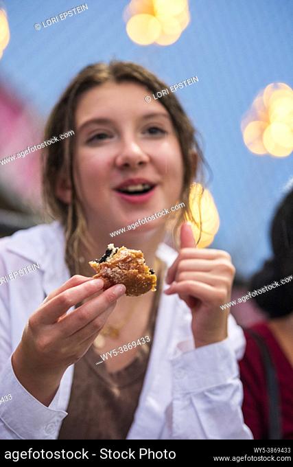 A caucasian teenage girl eats a deep-fried Oreo cookie at the county fair in Arlington, Virginia