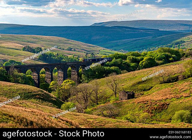 Near Cowgill, Cumbria, England, UK - May 16, 2019: A train passing the Dent Head Viaduct, with the Dent Dale landscape in the background