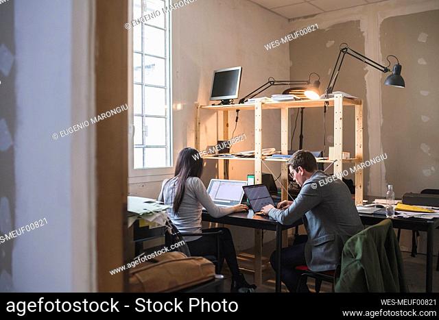 Businessman and woman using laptops at desk in office