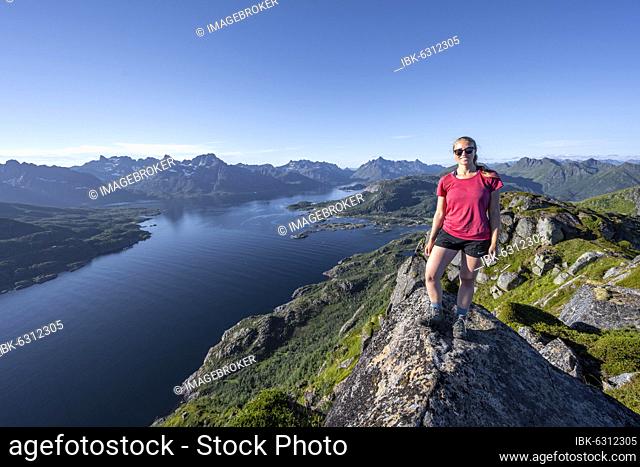 Young hiker standing on rocks, Fjord Raftsund and mountains, view from the top of Dronningsvarden or Stortinden, Vesterålen, Norway, Europe