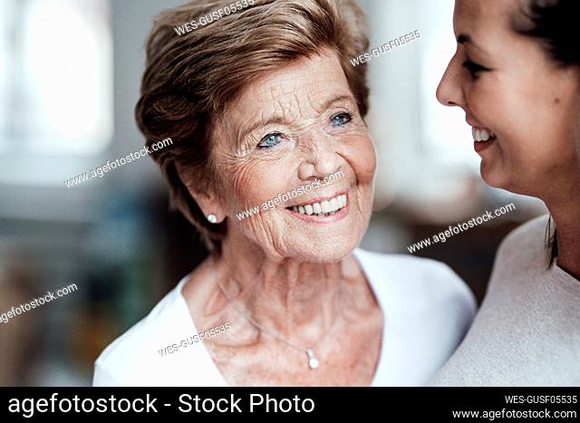 Happy senior woman looking away by smiling granddaughter at home