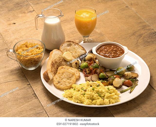 SCRAMBLED EGGS IN A CONTINENTAL BREAKFAST SERVED IN A WHITE PLATE ON WOODEN BACKGROUND