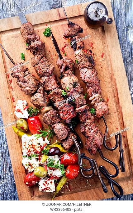 Traditional Greek Souvlaki on a barbecue skewer with feta and vegetable as top view on cutting board