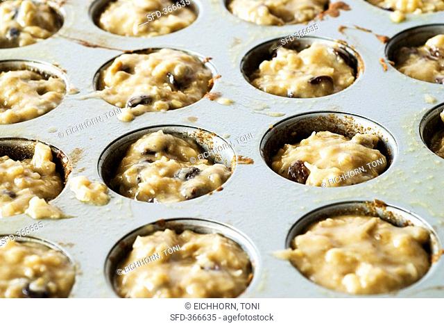 Holes in a muffin tin filled with raisin muffin mixture