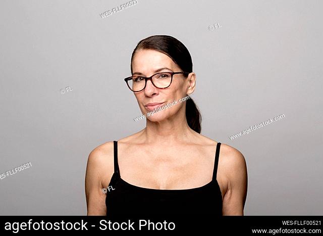 Smiling mature woman in black top wearing eyeglasses against gray background