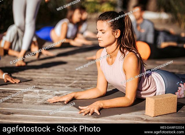 Woman with eyes closed lying on exercise mat while practicing yoga during sunny day