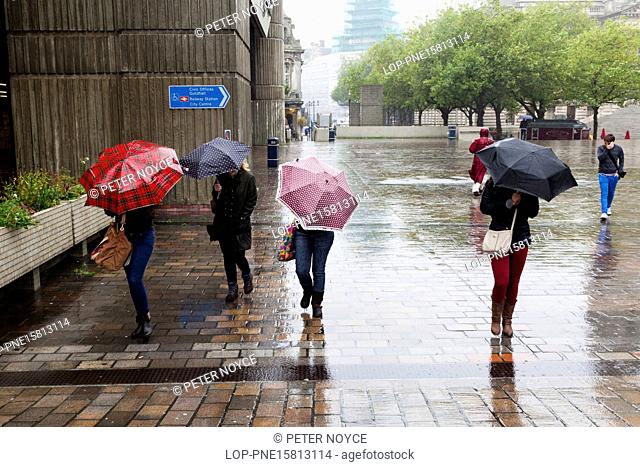 England, London, South Bank. Four women with umbrellas with heads down against the wind and rain