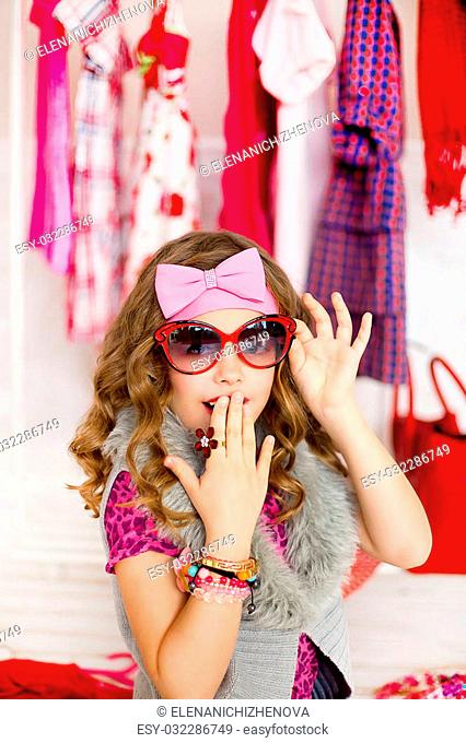 the little girl in red sunglasses and with a pink bow on the head near a mobile hanger tests joyful emotions