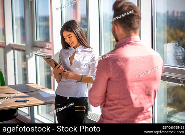 Confident businessman and businesswoman working in office interior. Beautiful lady looking at her tablet PC and smiling. Business concept