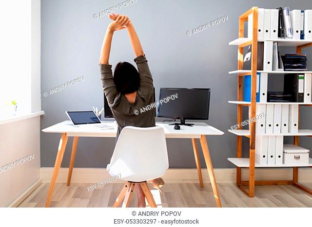 Rear View Of Young Businesswoman Stretching Her Arms In Office