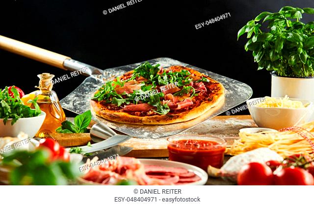 Freshly baked pizza on a metal paddle in a pizzeria with fresh ingredients in the foreground
